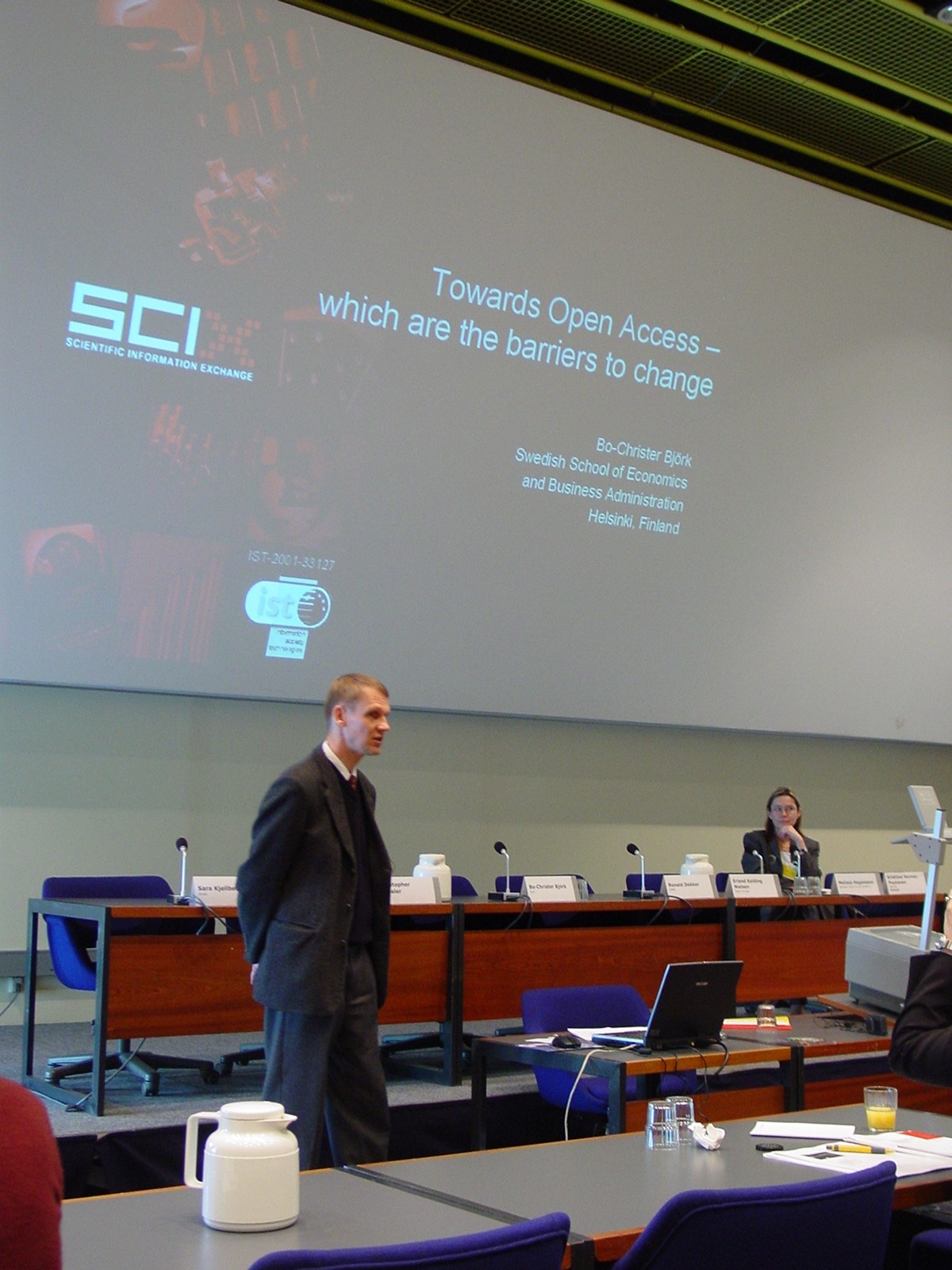 Bo-Christer Björk giving a lecture. Kristiina Hormia-Poutanen, chair of the session, sits behind the table.
