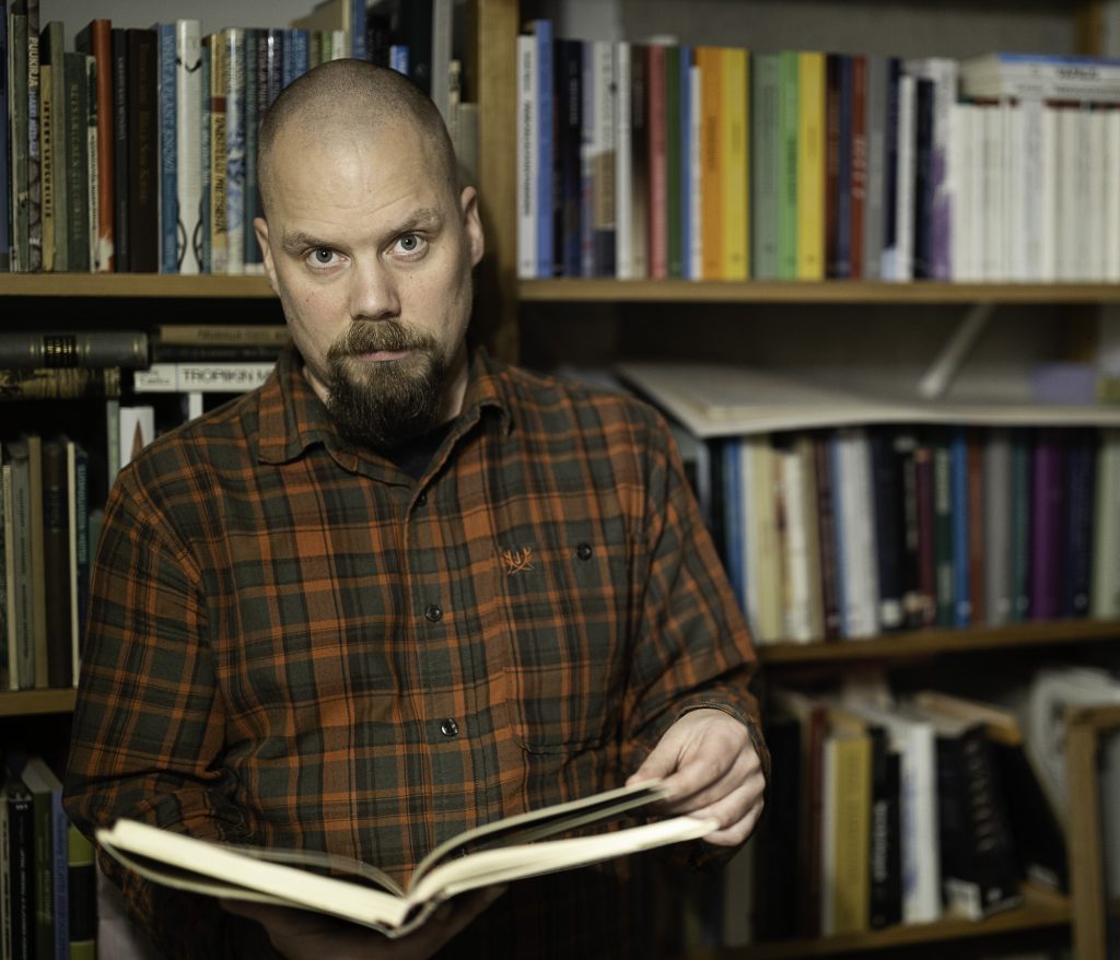 Filosofi Jukka Mikkonen selaa kirjaa kirjahyllyn edessä.
